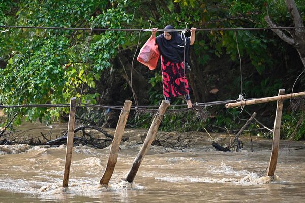 Женщина переходит реку по мосту, уничтоженному наводнением год назад в Сулевеси 