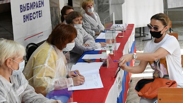 Девушка получает бюллетени для голосования на избирательном участке №33 в городе Абакане в Республике Хакасия