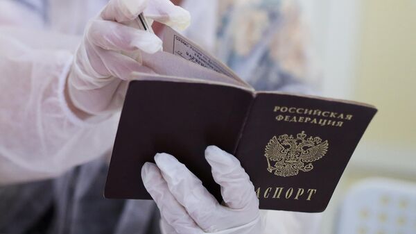 Сотрудница избирательного участка смотрит паспорт избирателя перед выдачей бюллетеня для голосования на выборах депутатов Государственной Думы РФ