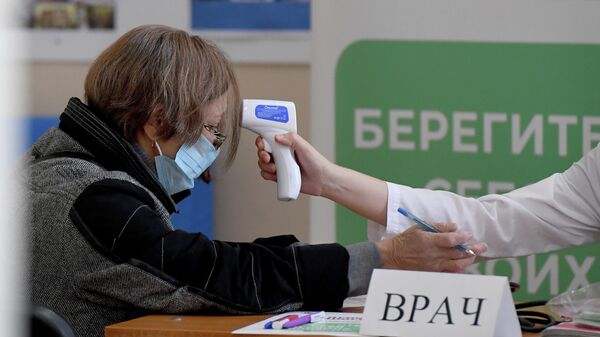 Медицинский работник измеряет температуру у женщины на пункте вакцинации от гриппа на избирательном участке № 42 в Казани, где проходят выборы депутатов Государственной Думы РФ