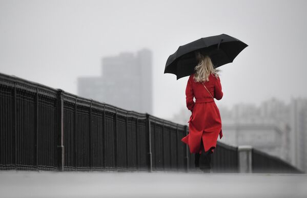 Женщина с зонтом идет по Крымскому мосту во время дождя в Москве