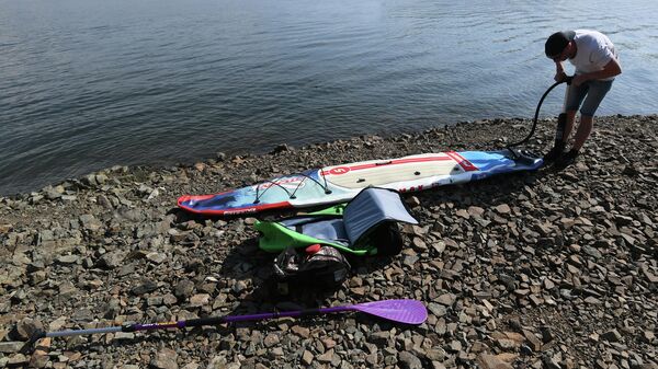 Мужчина накачивает насосом SUP-board на берегу Енисея