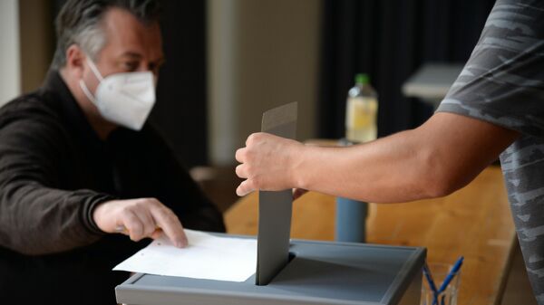  Мужчина опускает бюллетень в урну для голосования на одном из избирательных участков Потсдама во время голосования на выборах в Бундестаг