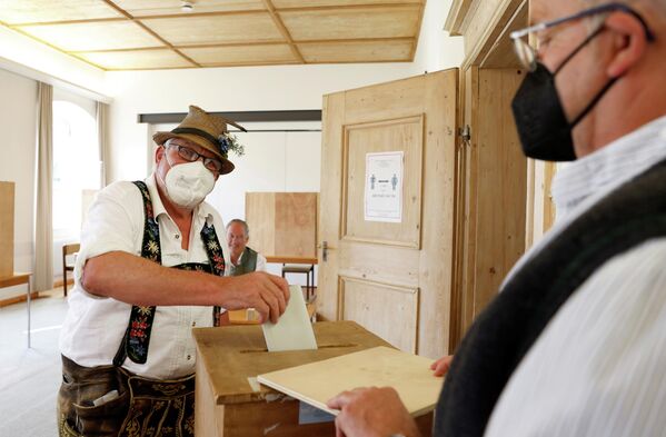 Мужчина в традиционном баварском костюме голосует на выборах в Бенедиктбойерн, Германия