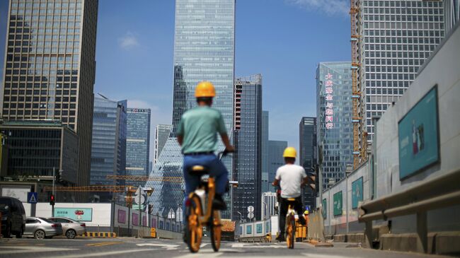 Мужчины проезжают на велосипедах мимо строительных площадок возле штаб-квартиры China Evergrande Group в Шэньчжэне, провинция Гуандун, Китай