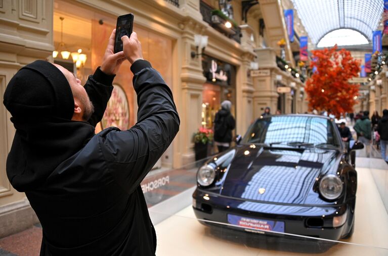 Мужчина фотографирует автомобиль Porsche 964 turbo, представленный на выставке редких спорткаров в ГУМе в рамках ГУМ Янгтаймер Ралли