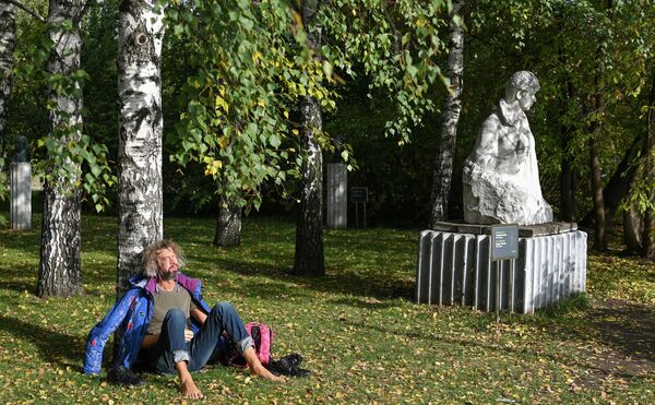 Мужчина сидит на солнце под деревом в парке искусств Музеон