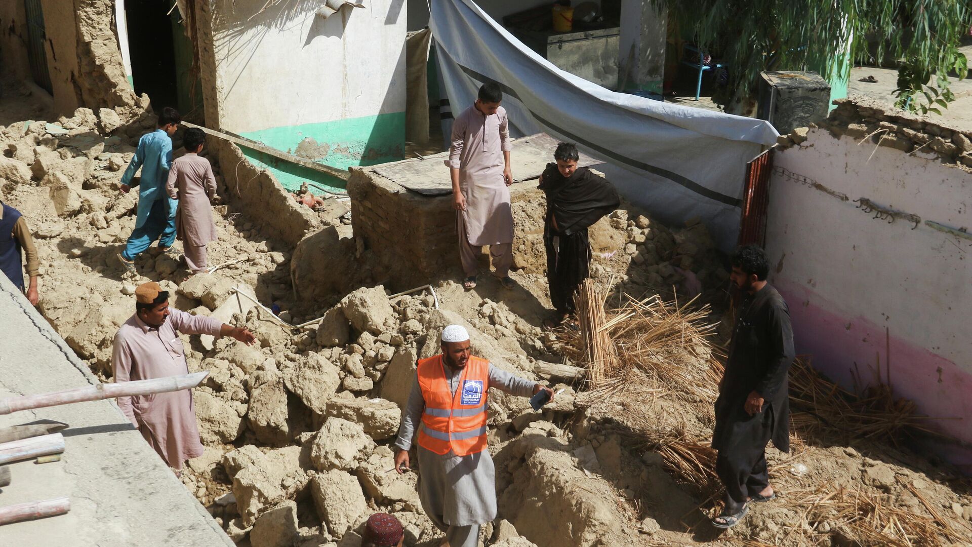 Спасатель и местные жители стоят среди обломков разрушенного дома после землетрясения в Харнае, провинция Белуджистан - РИА Новости, 1920, 07.10.2021