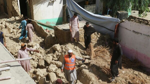 Спасатель и местные жители стоят среди обломков разрушенного дома после землетрясения в Харнае, провинция Белуджистан