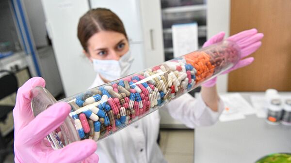 Сотрудница лаборатории держит колбу с муляжом капсульных таблеток