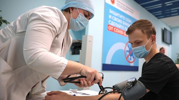 Медицинский работник измеряет давление молодому человеку перед вакцинацией