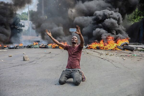 Мужчина фотографируется на фоне горящих шин во время протестов в Порт-о-Пренсе, Гаити 