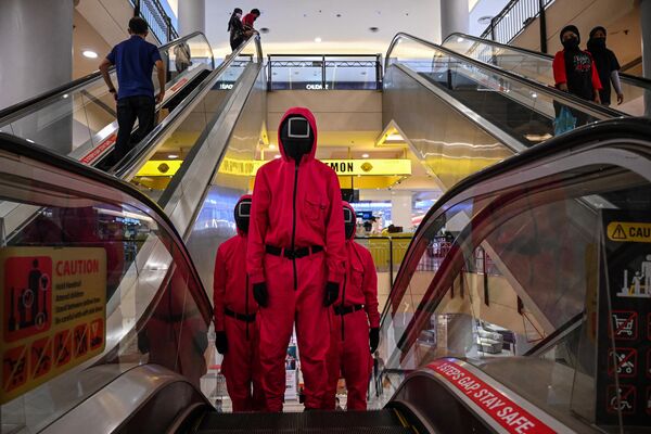 Косплееры, одетые в наряды из сериала Игра в кальмара, на эскалаторе в торговом центре в Куала-Лумпуре