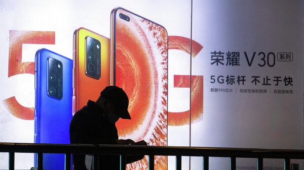 Мужчина стоит возле рекламы смартфонов 5G в Пекине