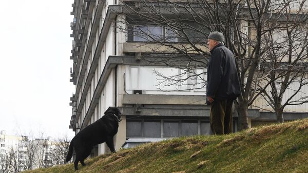 Мужчина выгуливает собаку рядом с жилым домом