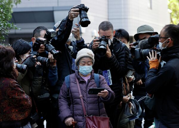 Фотографы снимают, как женщина смотрит пресс-конференцию принцессы Мако и ее мужа Кэя Комуро в Токио