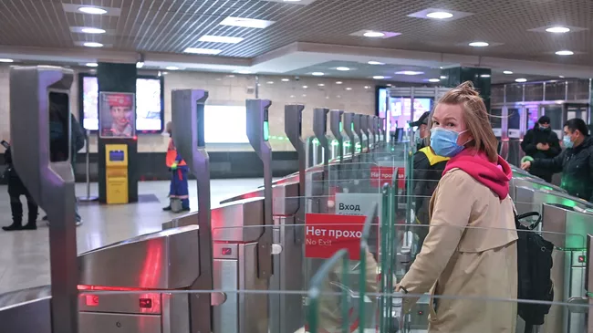 Пассажиры в защитных масках проходят через турникеты на станции метро