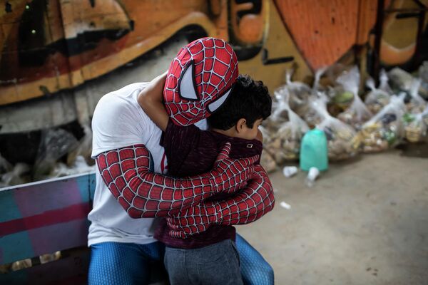 Волонтер в костюме человека-паука обнимает ребенка в фавеле в Рио-де-Жанейро 