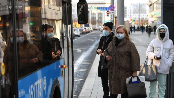 Пассажиры в защитных масках на остановке общественного транспорта в Москве