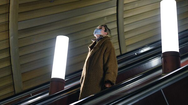 Женщина в защитной маске едет на эскалатора на станции Цветной бульвар Московского метрополитена