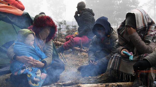 Женщины с детьми сидят у костра в лагере нелегальных мигрантов на белорусско-польской границе