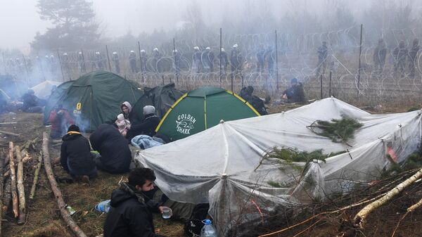 Беженцы возле заграждения из колючей проволоки в лагере нелегальных мигрантов на белорусско-польской границе