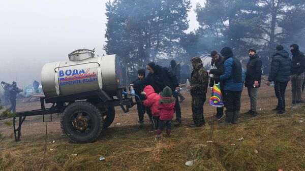 Беженцы стоят за питьевой водой в лагере нелегальных мигрантов на белорусско-польской границе