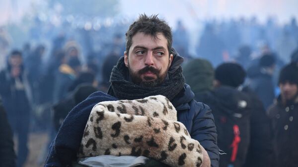 Беженец держит в руках теплые вещи в лагере нелегальных мигрантов на белорусско-польской границе