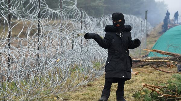 Девочка стоит возле заграждения из колючей проволоки в лагере нелегальных мигрантов на белорусско-польской границе