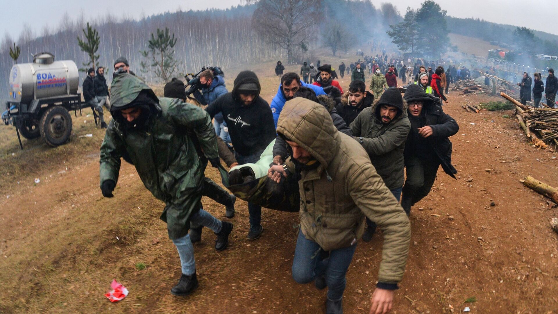 Мужчины несут к машине скорой помощи женщину в лагере нелегальных мигрантов на белорусско-польской границе - РИА Новости, 1920, 14.11.2021