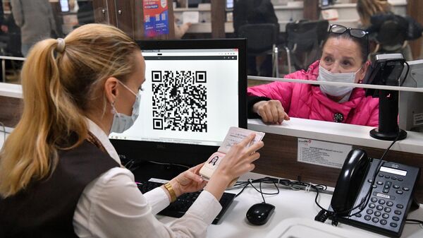 Сотрудница МФЦ проверяет документы у женщины для выдачи ей распечатанного бумажного QR-кода в многофункциональном центре госуслуг Мои документы в Москве