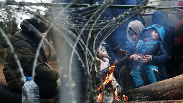 Беженцы греются у костра в лагере нелегальных мигрантов неподалеку от пункта пропуска Брузги на белорусско-польской границе