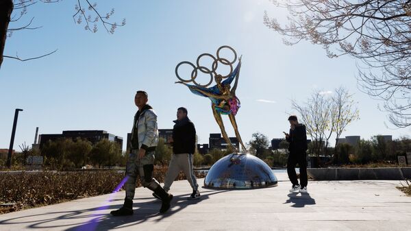 Люди проходя мимо скульптуры в виде олимпийских колец в Пекине