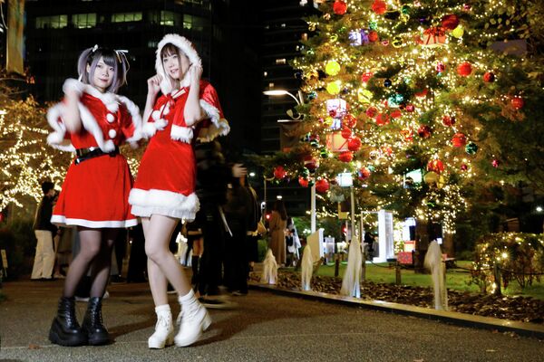 Женщины в костюмах Санта-Клауса фотографируются на фоне рождественских иллюминаций в Токио, Япония
