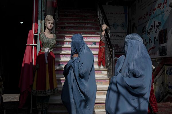 Афганские женщины в бурках проходят мимо магазина одежды в Герате, Афганистан