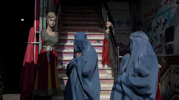 Афганские женщины в бурках проходят мимо магазина одежды в Герате, Афганистан