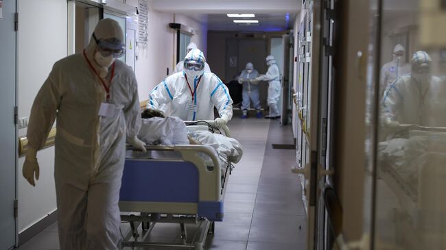 Медицинские работники везут пациента на носилках по коридору COVID-госпиталя