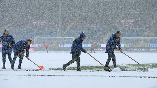 Ground staff clear snow from the pitch as the snow falls ahead of the English Premier League football match between Burnley and Tottenham Hotspur at Turf Moor in Burnley, north west England on November 28, 2021. - The game has since been postponed due to the weather. (Photo by Lindsey Parnaby / AFP) / RESTRICTED TO EDITORIAL USE. No use with unauthorized audio, video, data, fixture lists, club/league logos or 'live' services. Online in-match use limited to 120 images. An additional 40 images may be used in extra time. No video emulation. Social media in-match use limited to 120 images. An additional 40 images may be used in extra time. No use in betting publications, games or single club/league/player publications. / 