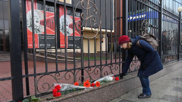 Девушка возлагает цветы к зданию театра Градский холл в Москве