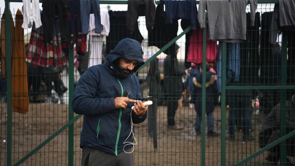 Мужчина смотрит мобильный телефон в центре временного содержания мигрантов, оборудованном в логистическом центре в пункте пропуска Брузги, на белорусско-польской границе