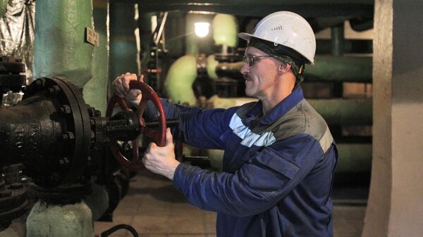 Рабочий поворачивает вентиль на трубах в котельной в подвале жилого многоквартирного дома в Москве
