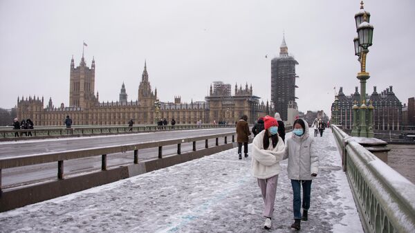 Люди в защитных масках гуляют во время снегопада в Лондоне