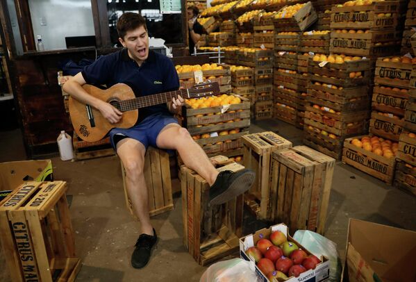 Музыкант играет на гитаре в ожидании покупателей в овощном магазине в Росарио, Аргентина 