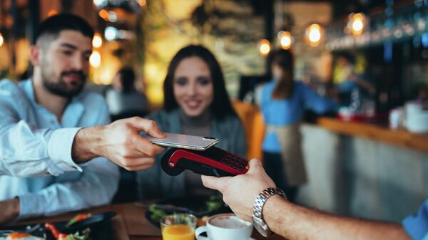 Мужчина оплачивает счет в ресторане с помощью мобильного телефона