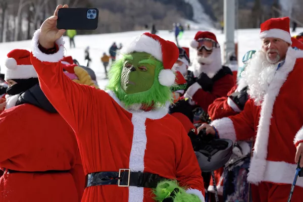 Лыжник, одетый как Гринч, делает селфи во время благотворительного заезда Санта-Клаусов на горнолыжном курорте Бетел в США