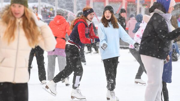 Люди катаются на коньках на площадке ГУМ-катка в Москве во время снегопада