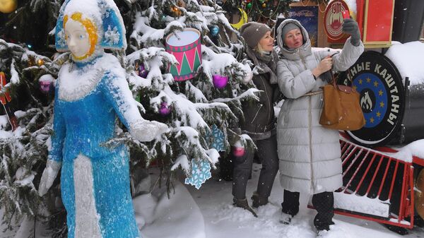 Девушки фотографируются на фоне новогодней елки у ГУМа в Москве во время снегопада