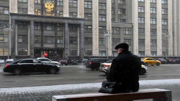 Мужчина сидит на скамейке напротив здания Государственной Думы РФ