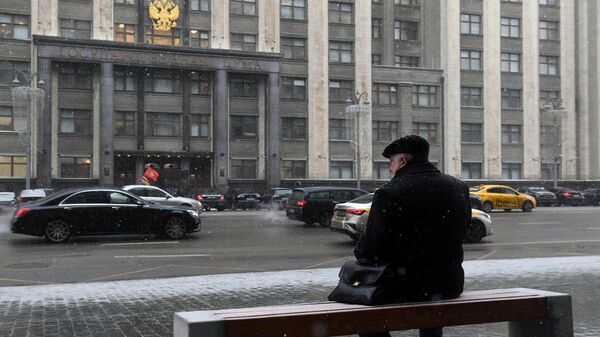 Мужчина сидит на скамейке напротив здания Государственной Думы РФ