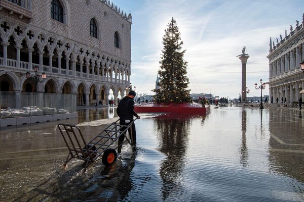 Мужчина с тележкой на площади Сан-Марко, затопленной морским приливом, Венеция, Италия